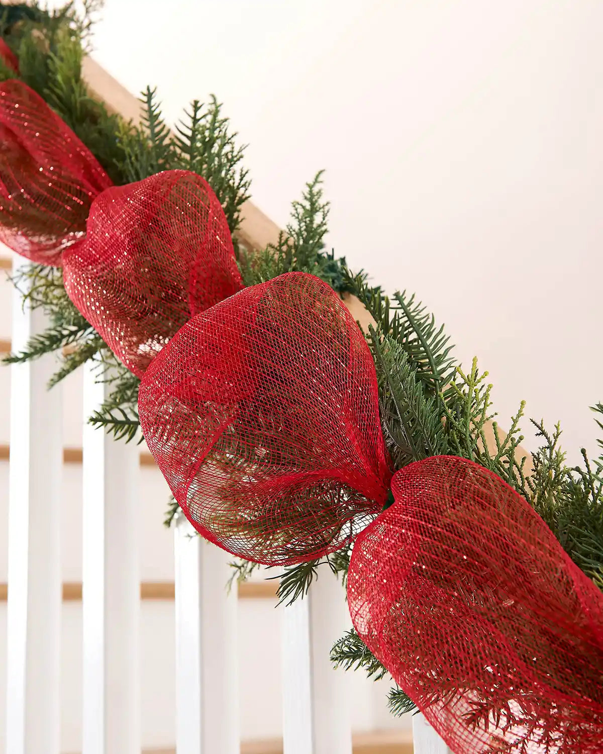 Decorative garland on a staircase banister with red mesh ribbon against a cream background