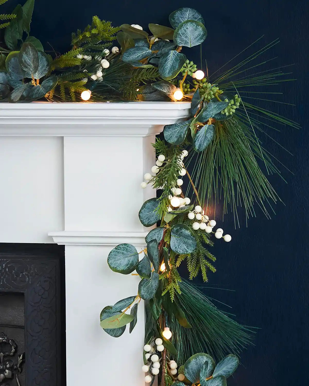 Decorative garland with Berries & Eucalyptuses, lights on a white fireplace mantel against a dark background