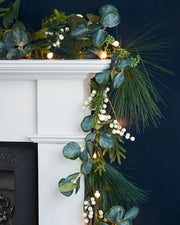 Decorative garland with Berries & Eucalyptuses, lights on a white fireplace mantel against a dark background