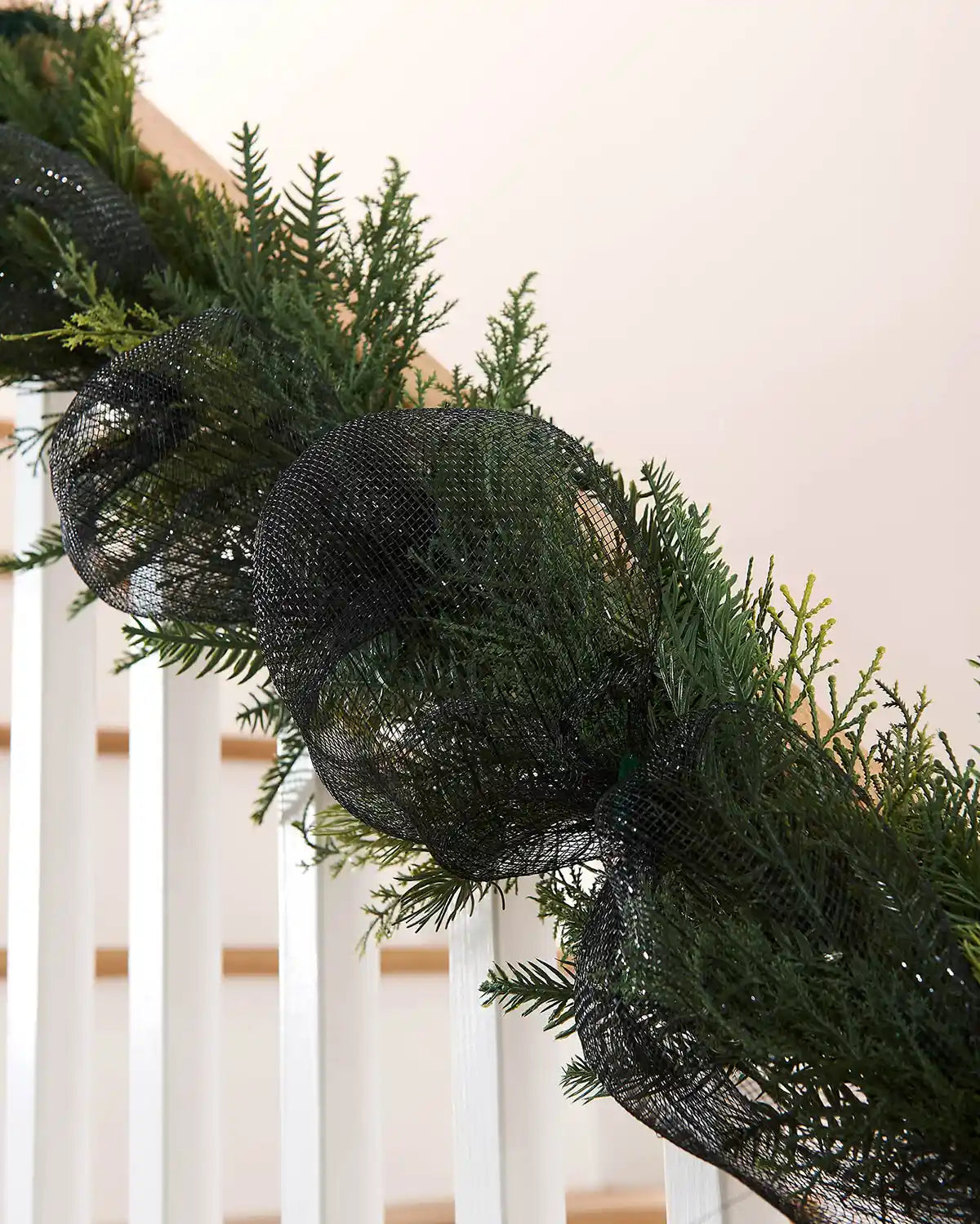 Decorative garland with black mesh ribbon on a wooden staircase banister against a cream wall