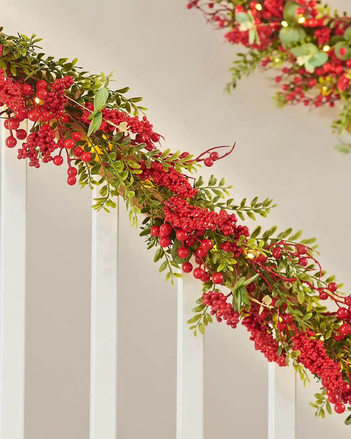 Decorative garland with red berries and green leaves on a neutral background