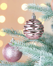 Decorative glitter and textured  pink baubles on a Christmas tree with blurred lights in the background