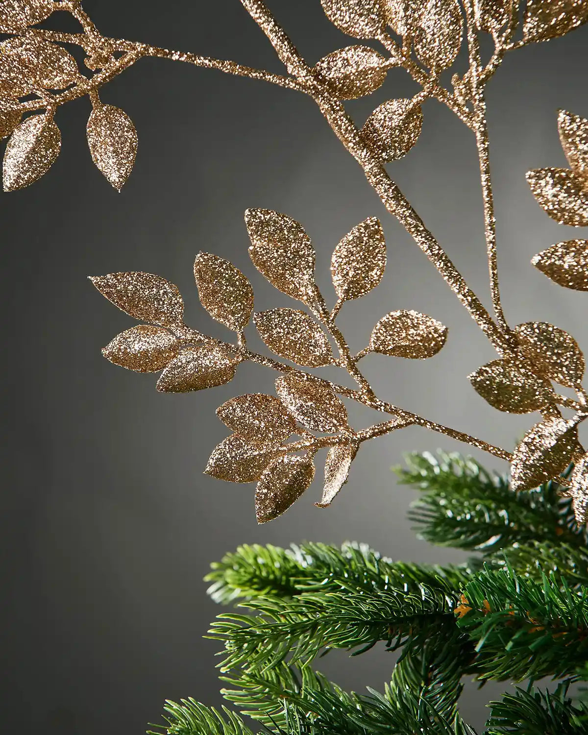 Decorative glitter gold branch with leaves on a grey background and a Christmas tree