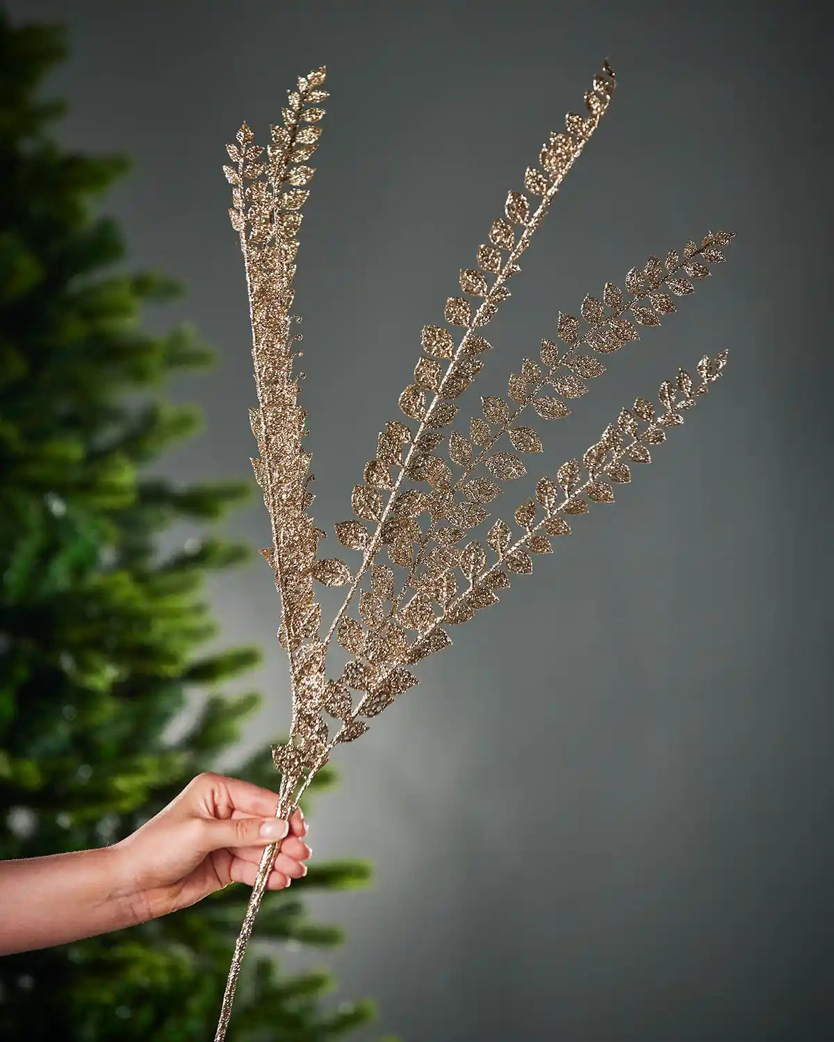 Decorative glitter gold fern branch held by a hand against a grey background
