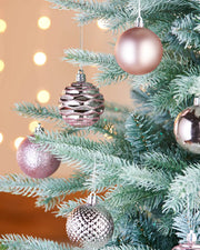 Decorative glitter, matt and textured pink baubles on a Christmas tree with blurred lights in the background
