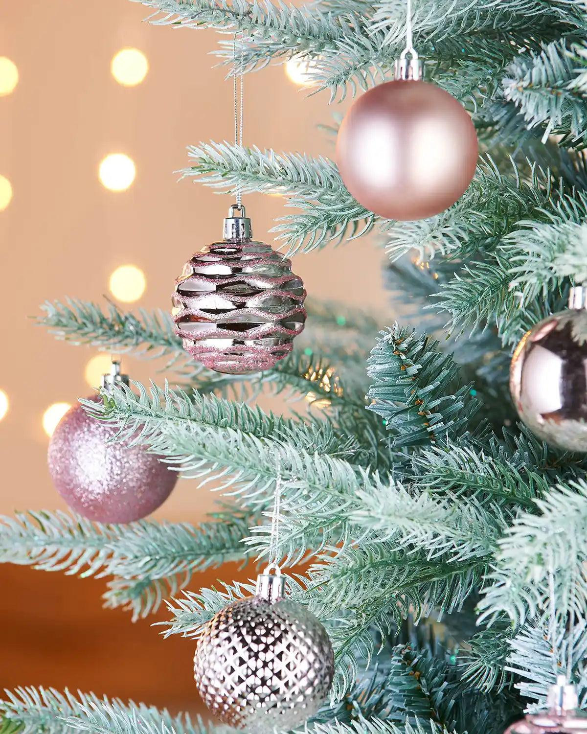 Decorative glitter, matt and textured pink baubles on a Christmas tree with blurred lights in the background