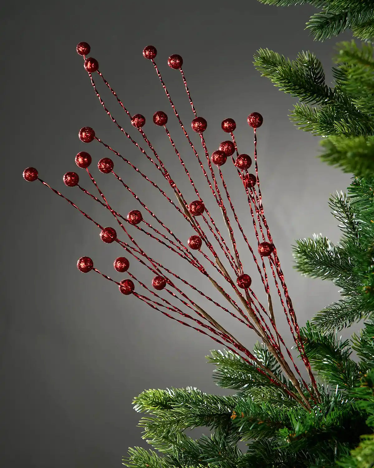 Decorative glitter red berry branch on a Christmas tree against a grey background