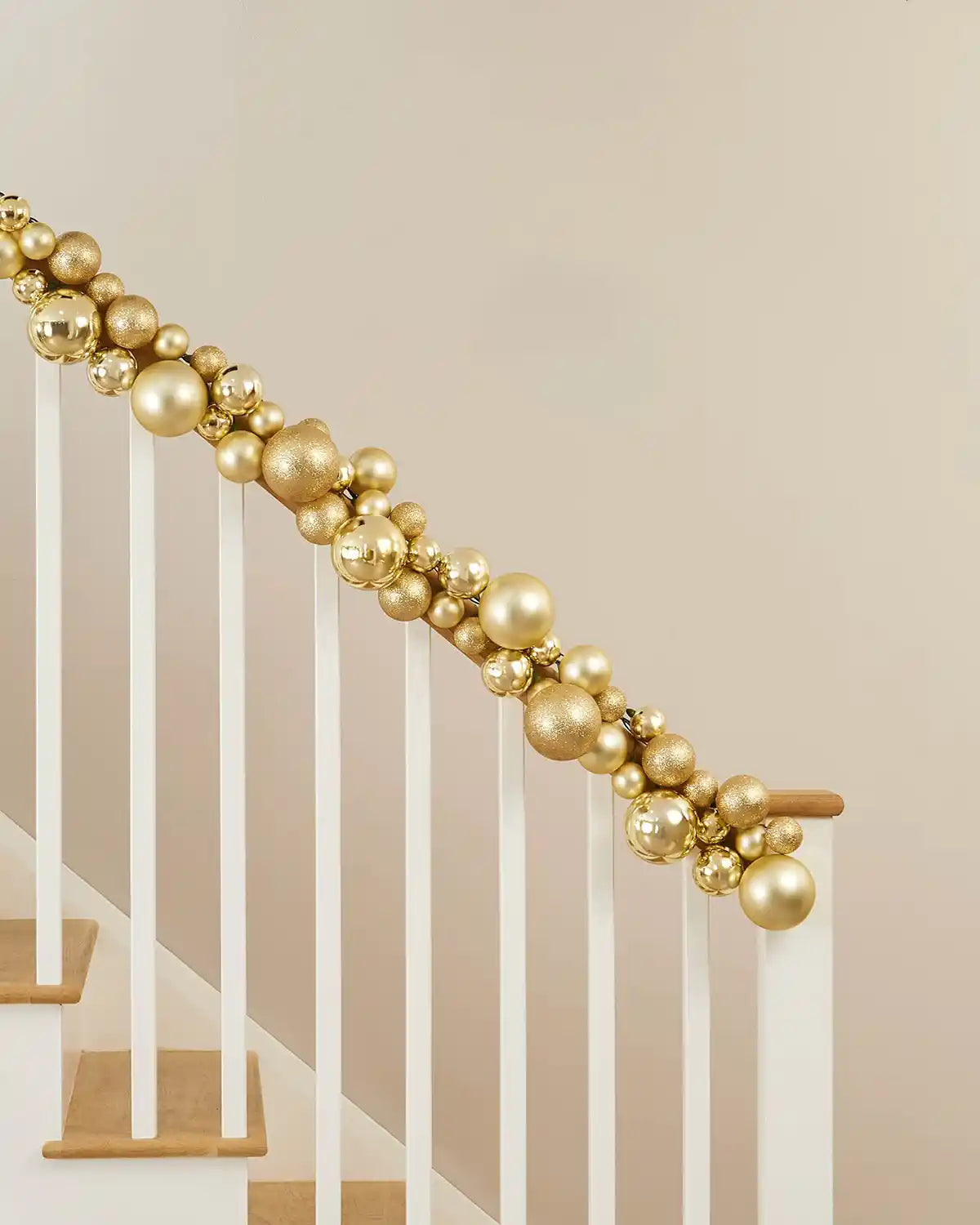 Decorative gold bauble garland on a staircase railing against a beige wall.