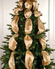 Decorative gold ribbons on a Christmas tree against a white wall.