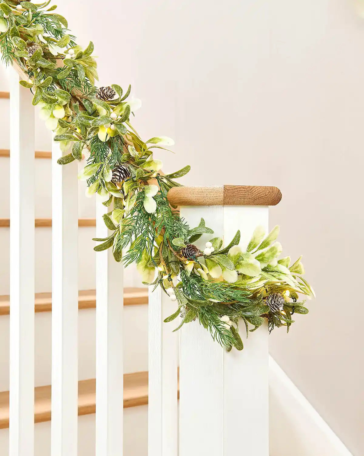 Decorative green garland with pinecones and white berries on a staircase banister against a beige background