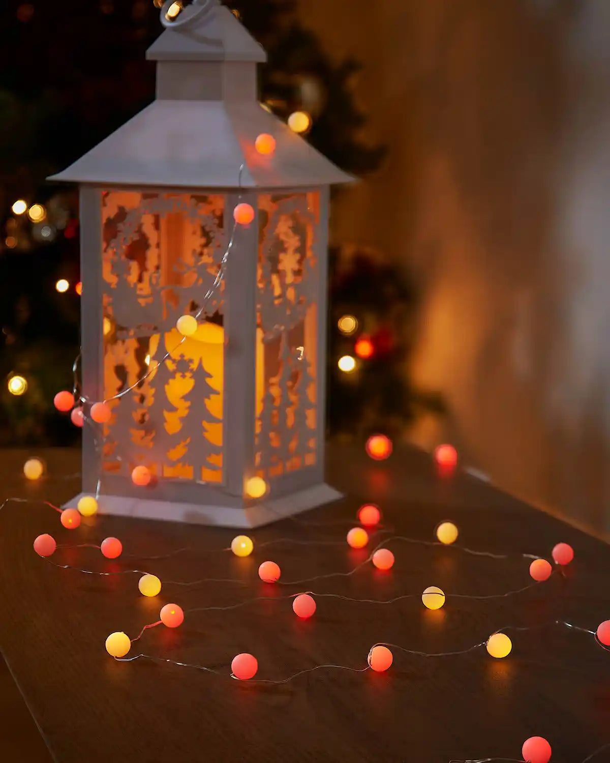 Decorative lantern with yellow and orange berry string lights on a table with a blurred background