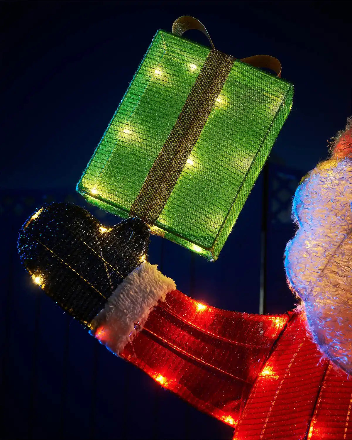 Decorative light-up gift box with LED lights held by a gloved hand against a dark background