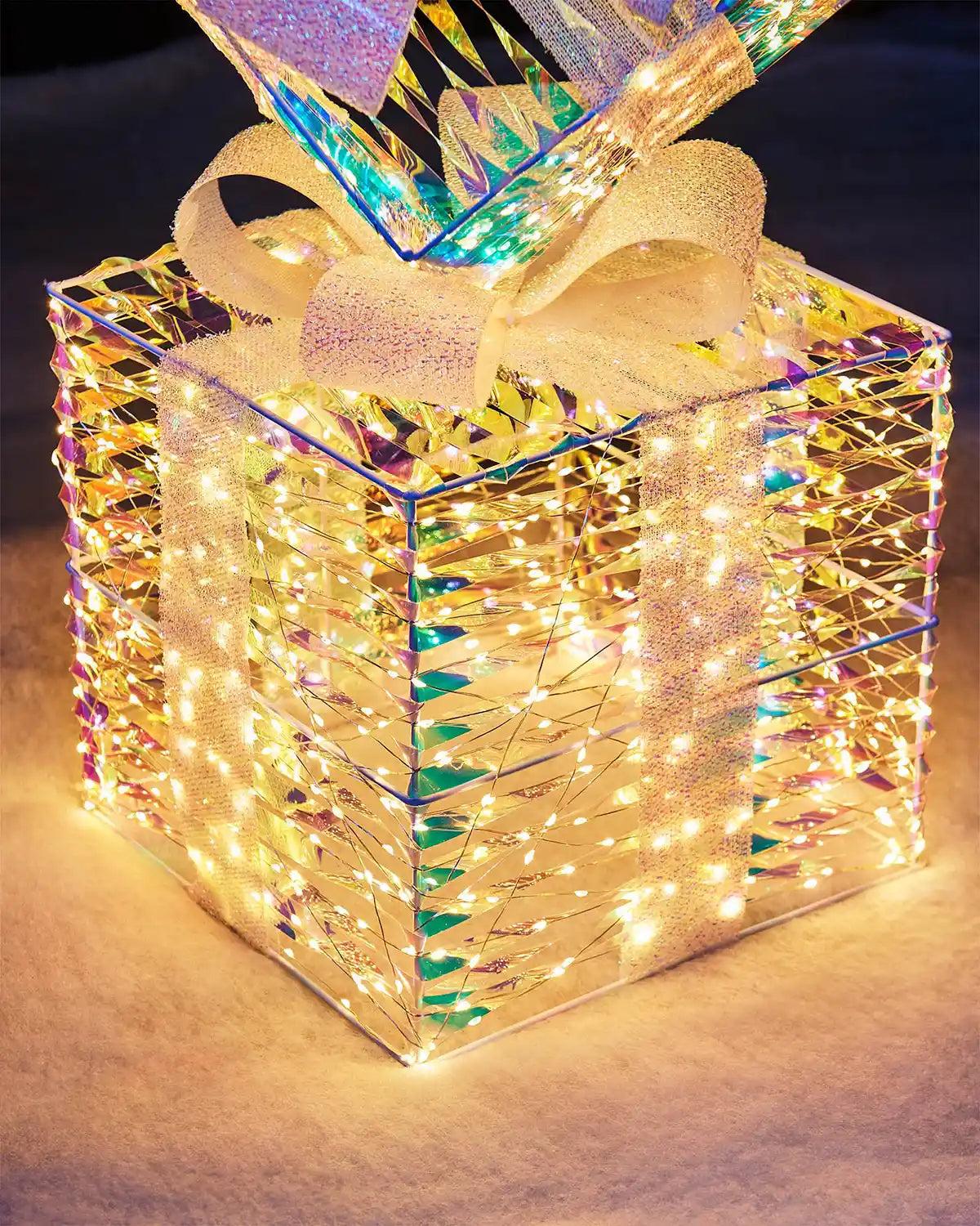 Decorative light-up gift iridescent  box with LED lights and a white bow on a dark background.