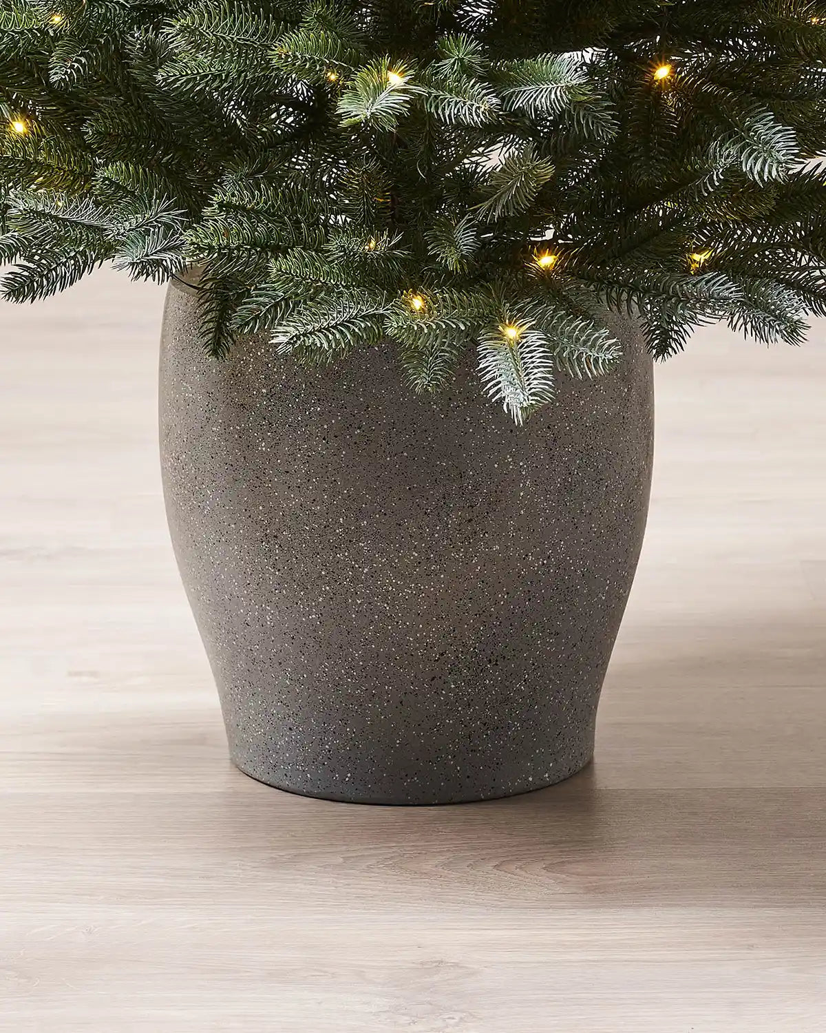Decorative pot with a Christmas tree and lights on a wooden floor