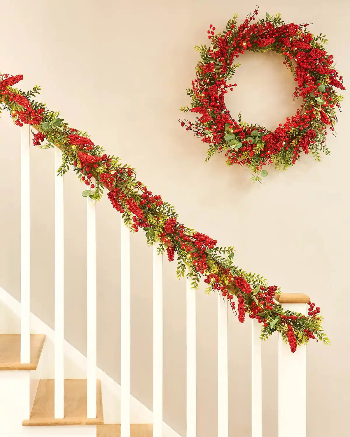 Decorative red berry garland and matching wreath on a staircase with a neutral wall background.