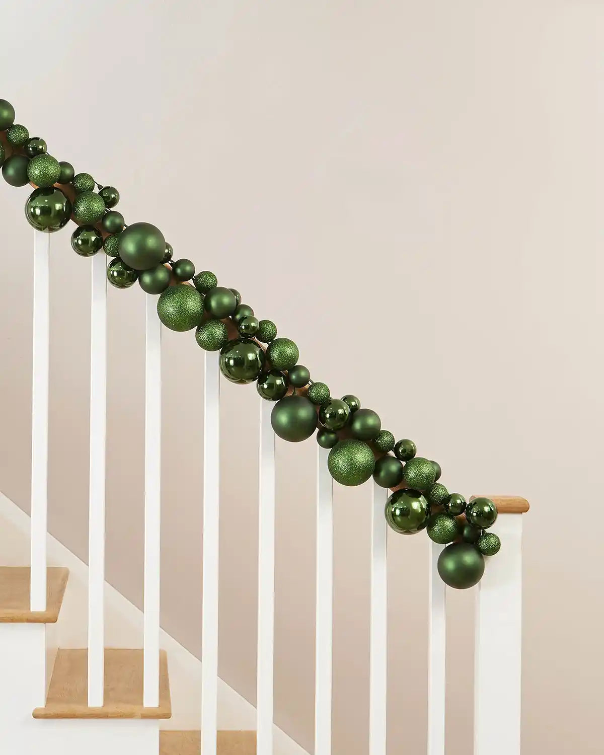 Decorative sage green bauble garland on a staircase railing against a beige wall.