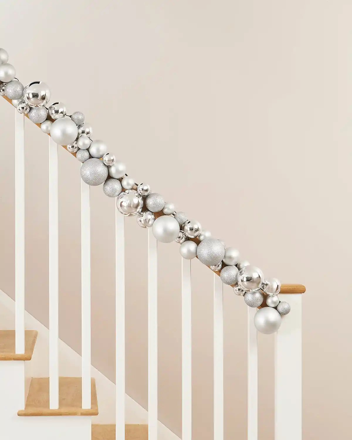 Decorative silver bauble garland on a staircase railing against a beige wall.