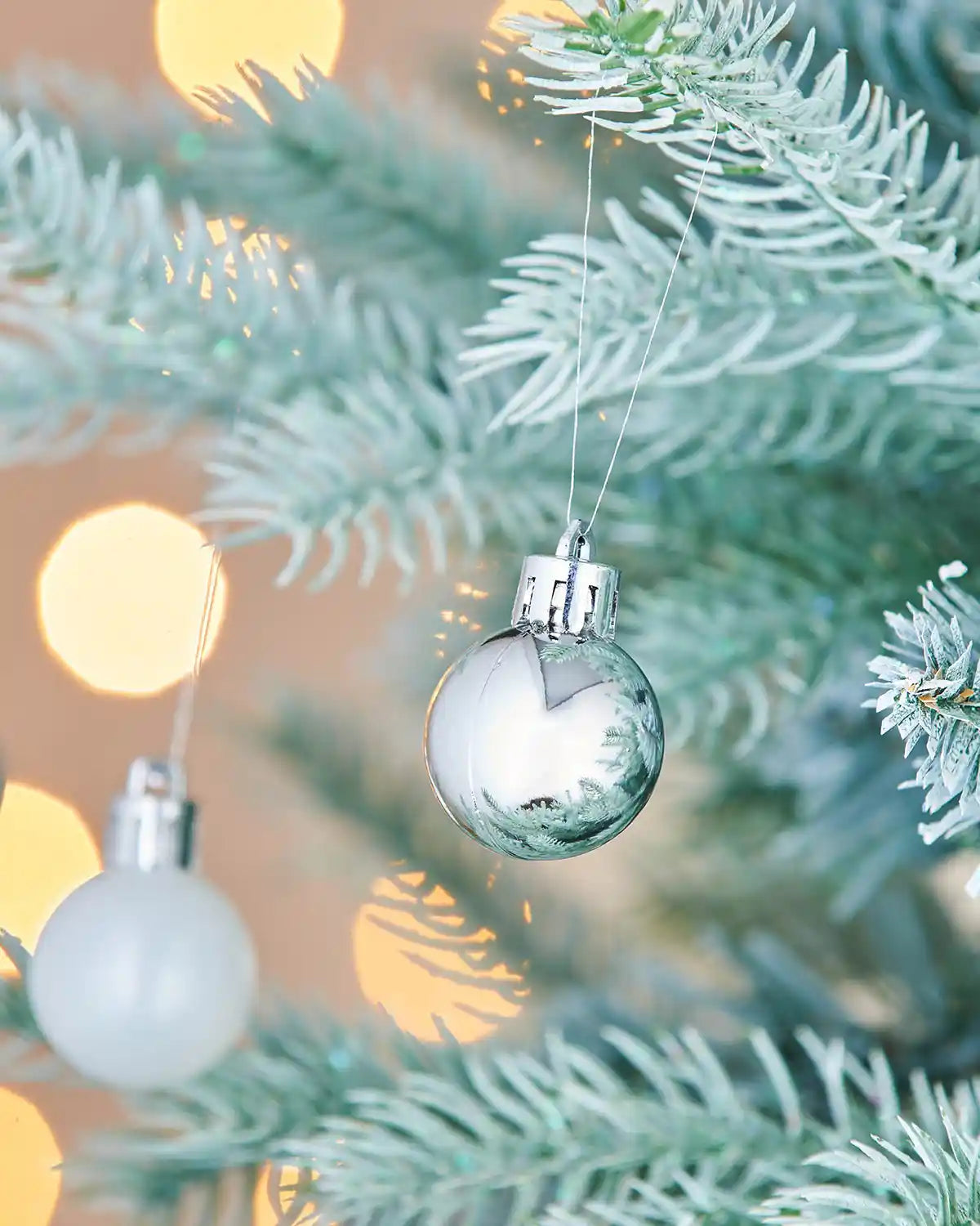 Decorative silver glass baubles hanging on a Christmas tree with blurred lights in the background