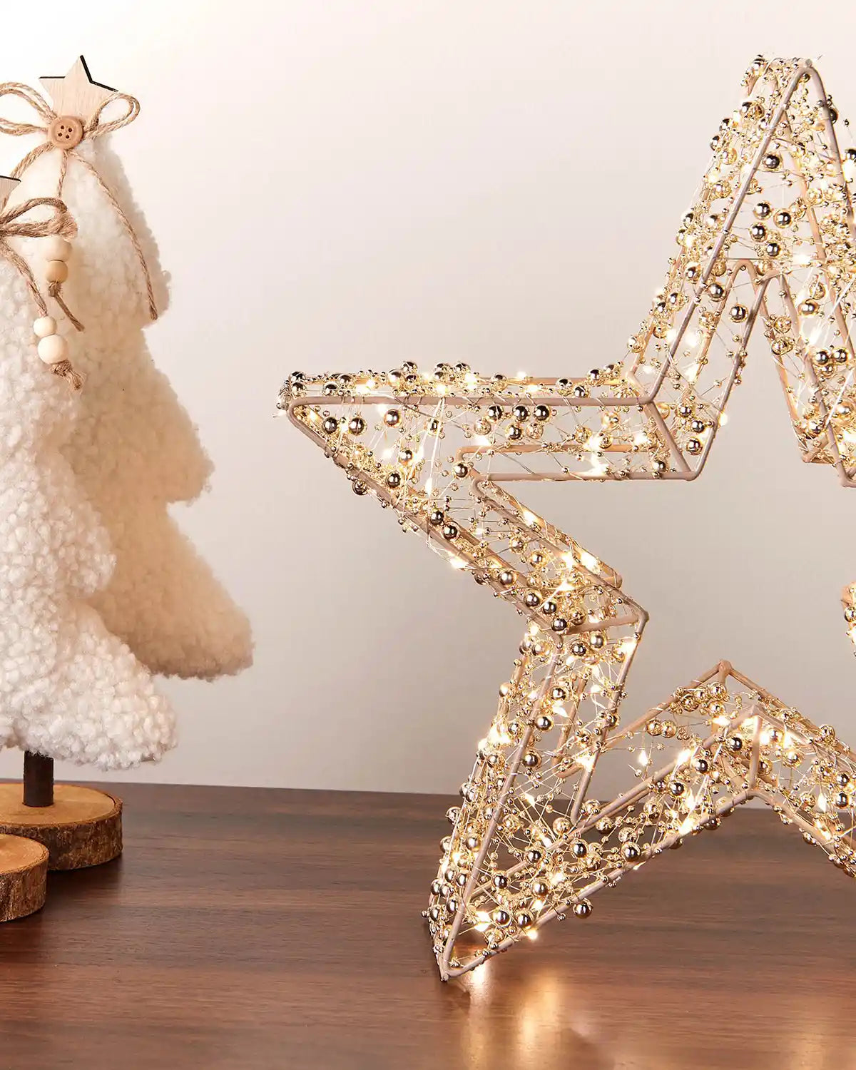 Decorative star-shaped light fixture on a wooden surface with a neutral background and small sherpa trees on wooden stands