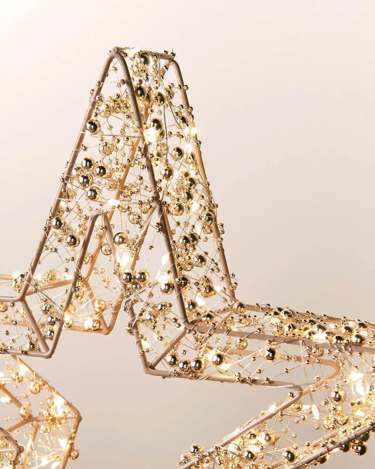 Decorative star made of gold beads and Copper wire with warm white LEDs on a light background