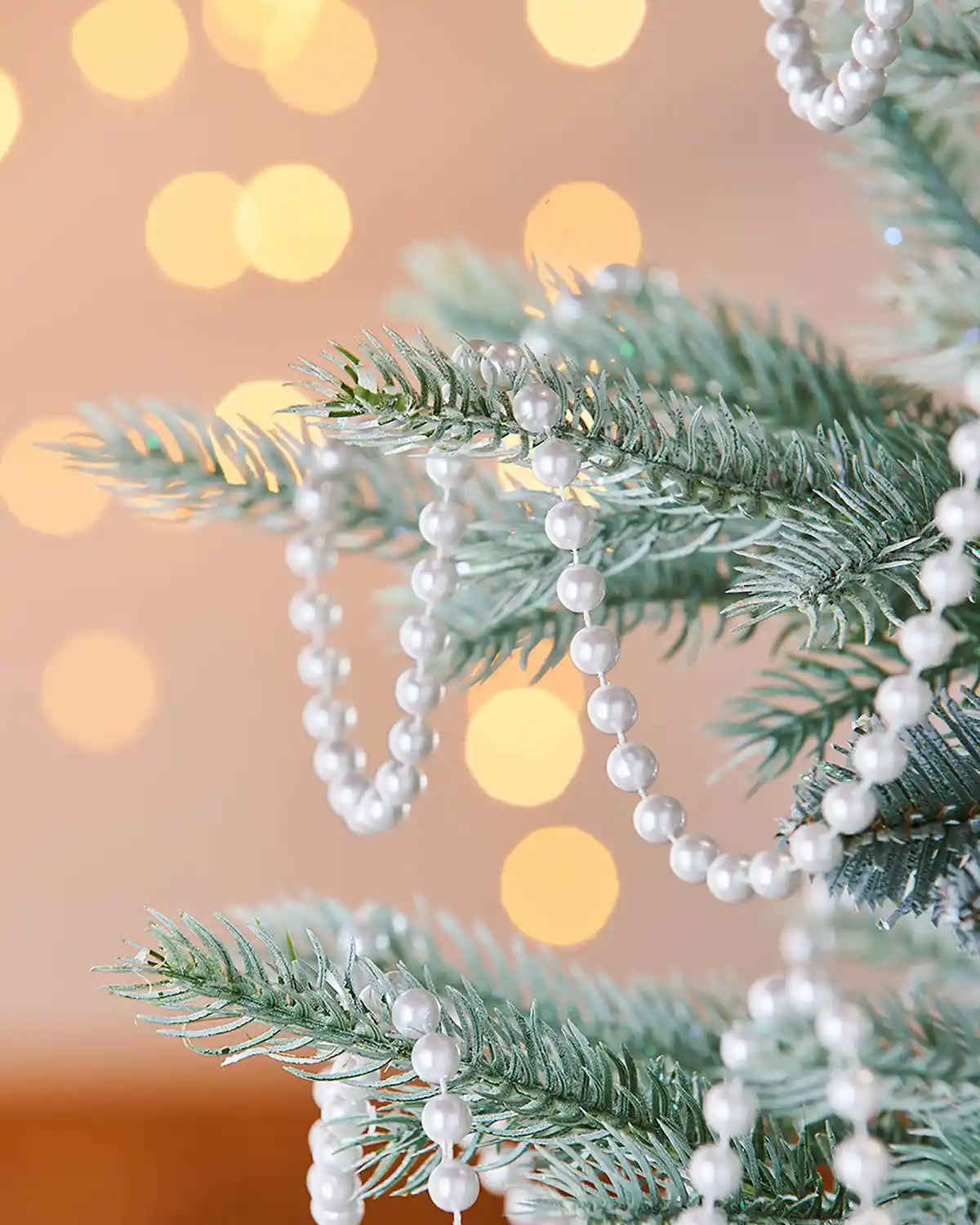 Decorative string of white beaded garland on a Christmas tree with a blurred lights in background