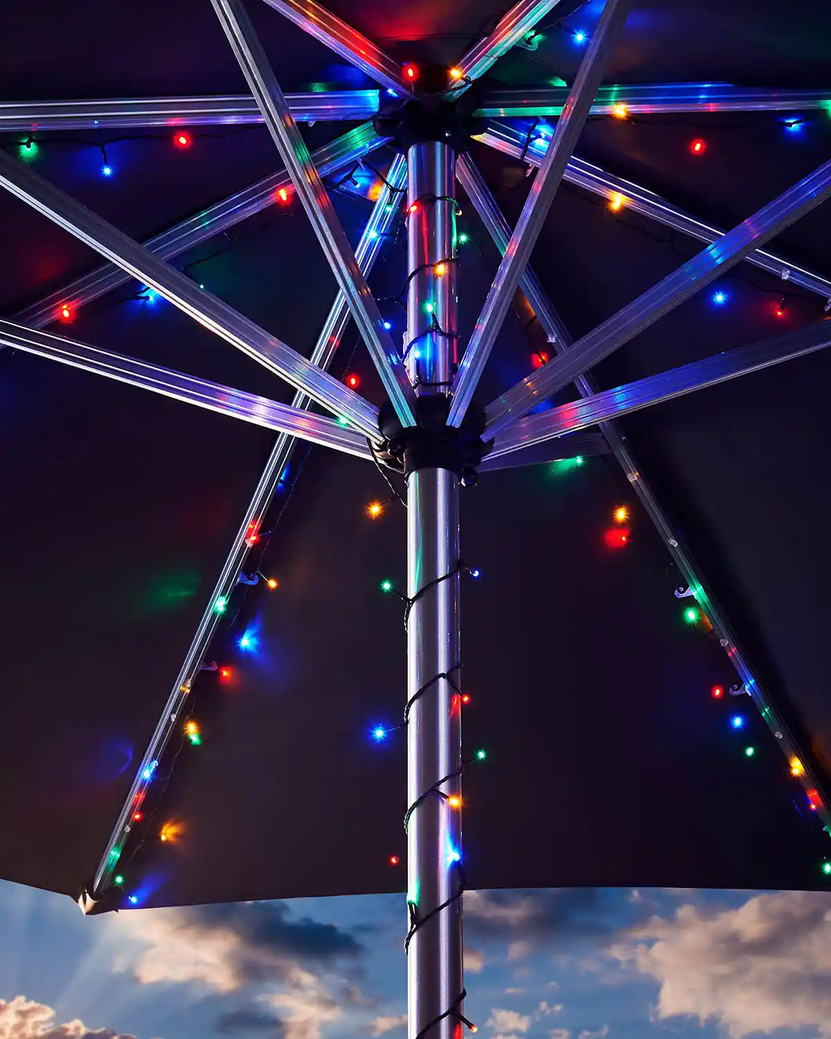 Decorative umbrella pole with multi colour fairy lights against a cloudy sky 