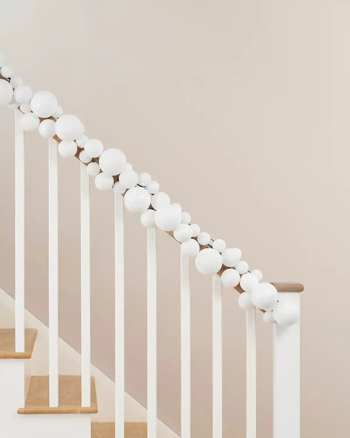 Decorative white bauble garland on a staircase railing against a beige wall.
