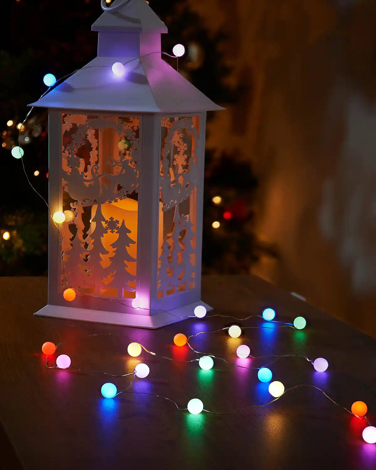 Decorative white lantern with multi coloured string berry lights on a dark surface