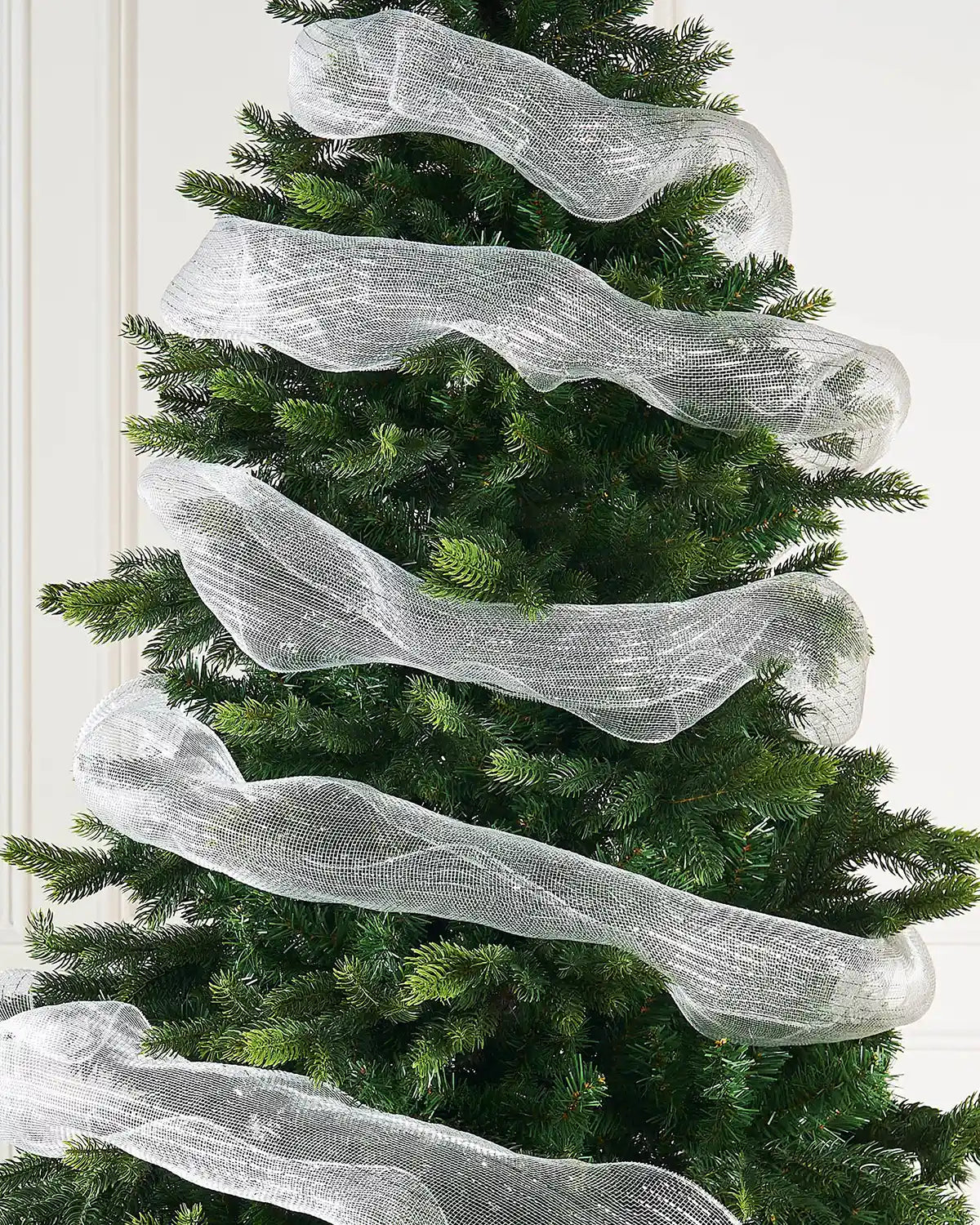 Decorative white mesh ribbon on a Christmas tree against a cream wall