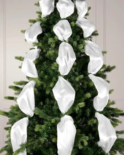 Decorative white ribbons on a Christmas tree against a neutral wall.