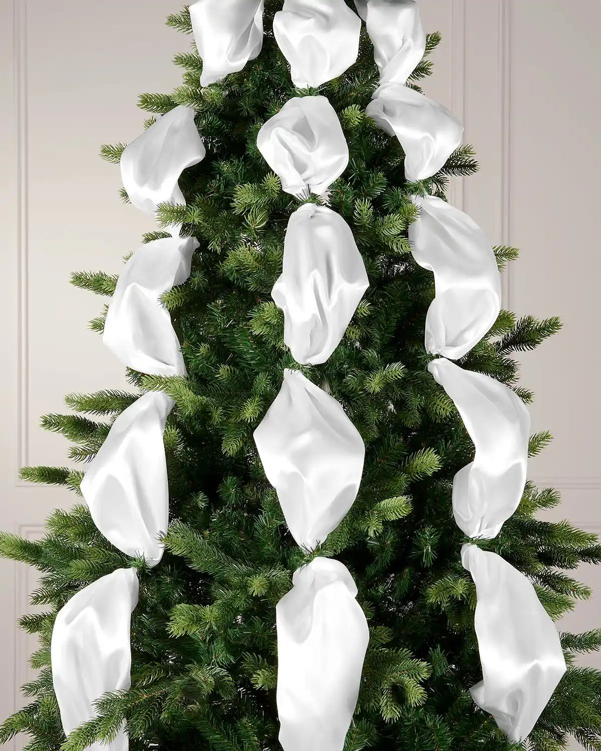Decorative white ribbons on a Christmas tree against a neutral wall.