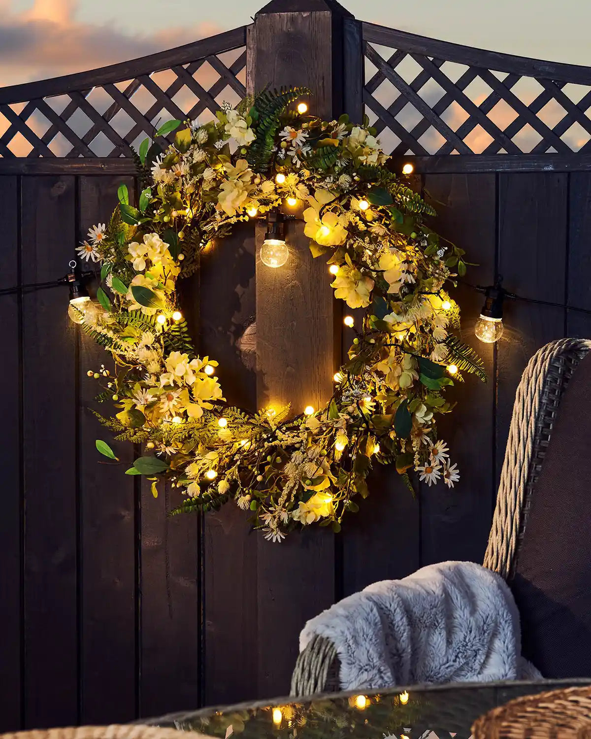 Decorative wreath with berry lights and a candle on a wooden wall.