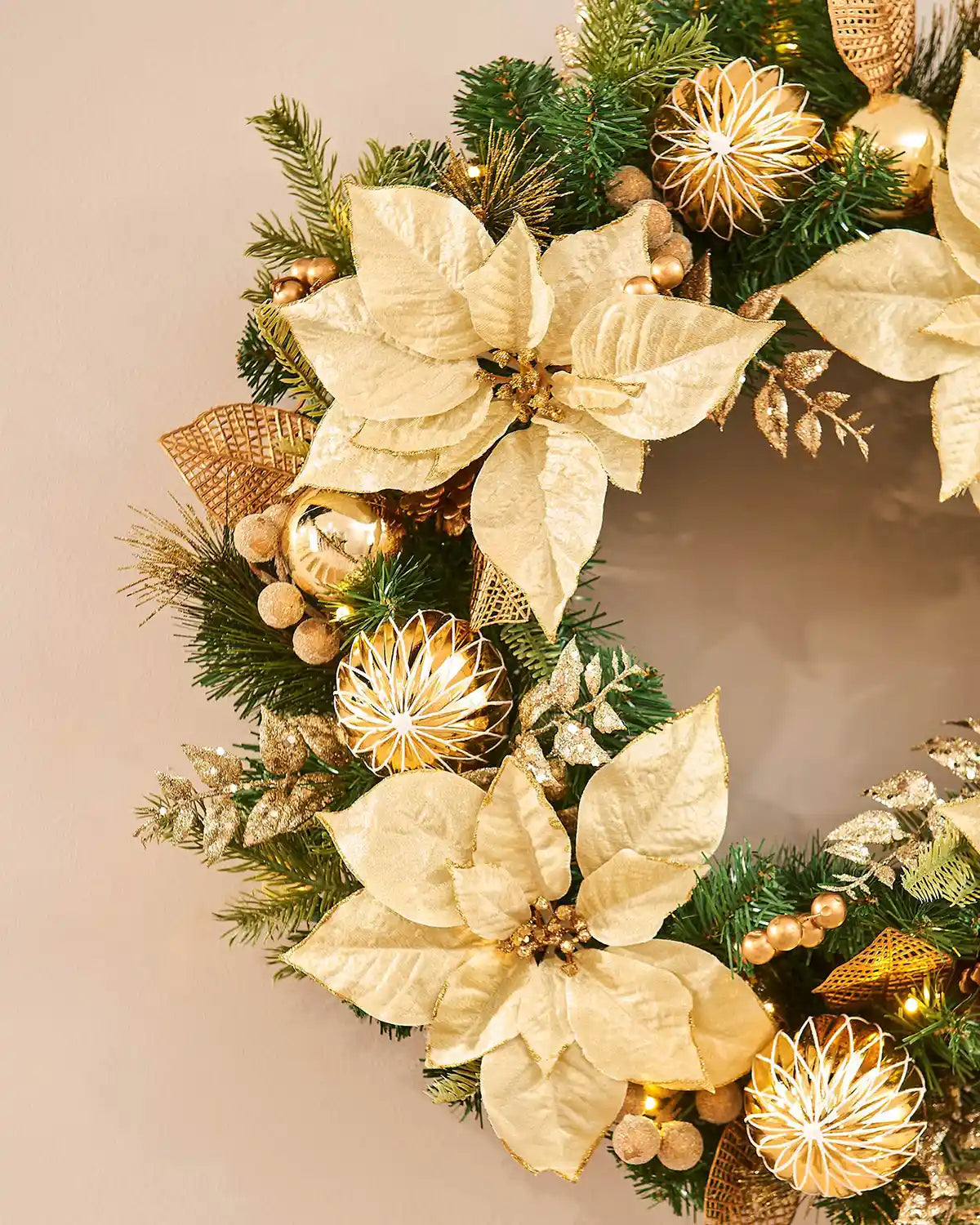 Decorative wreath with gold poinsettias and ornaments on a beige background