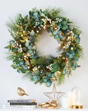 Decorative wreath with greenery, Eucalyptus and lights on a white wall with books, candles and gold ornaments 