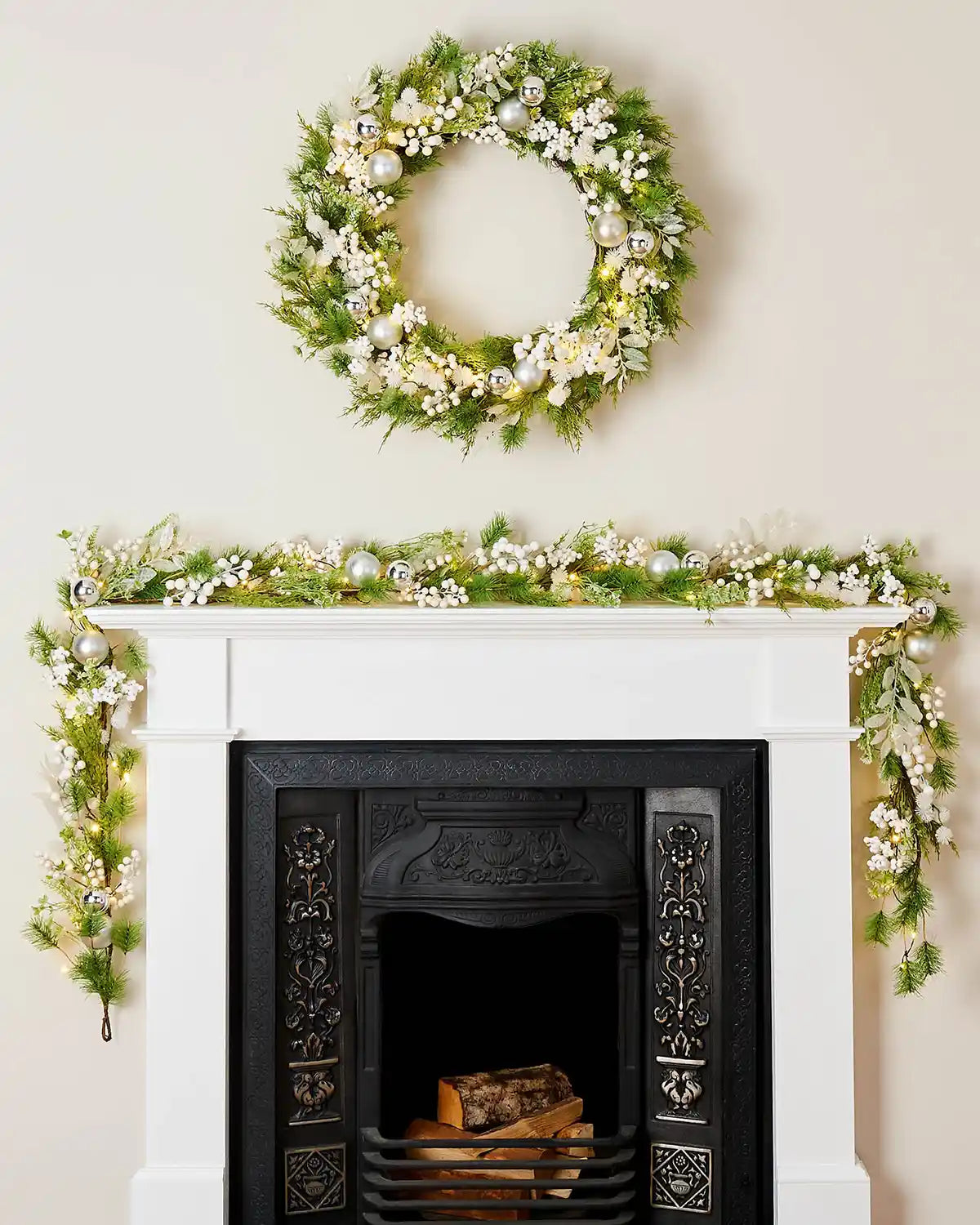 Decorative wreath with matching  garland on a fireplace mantel against a cream wall.