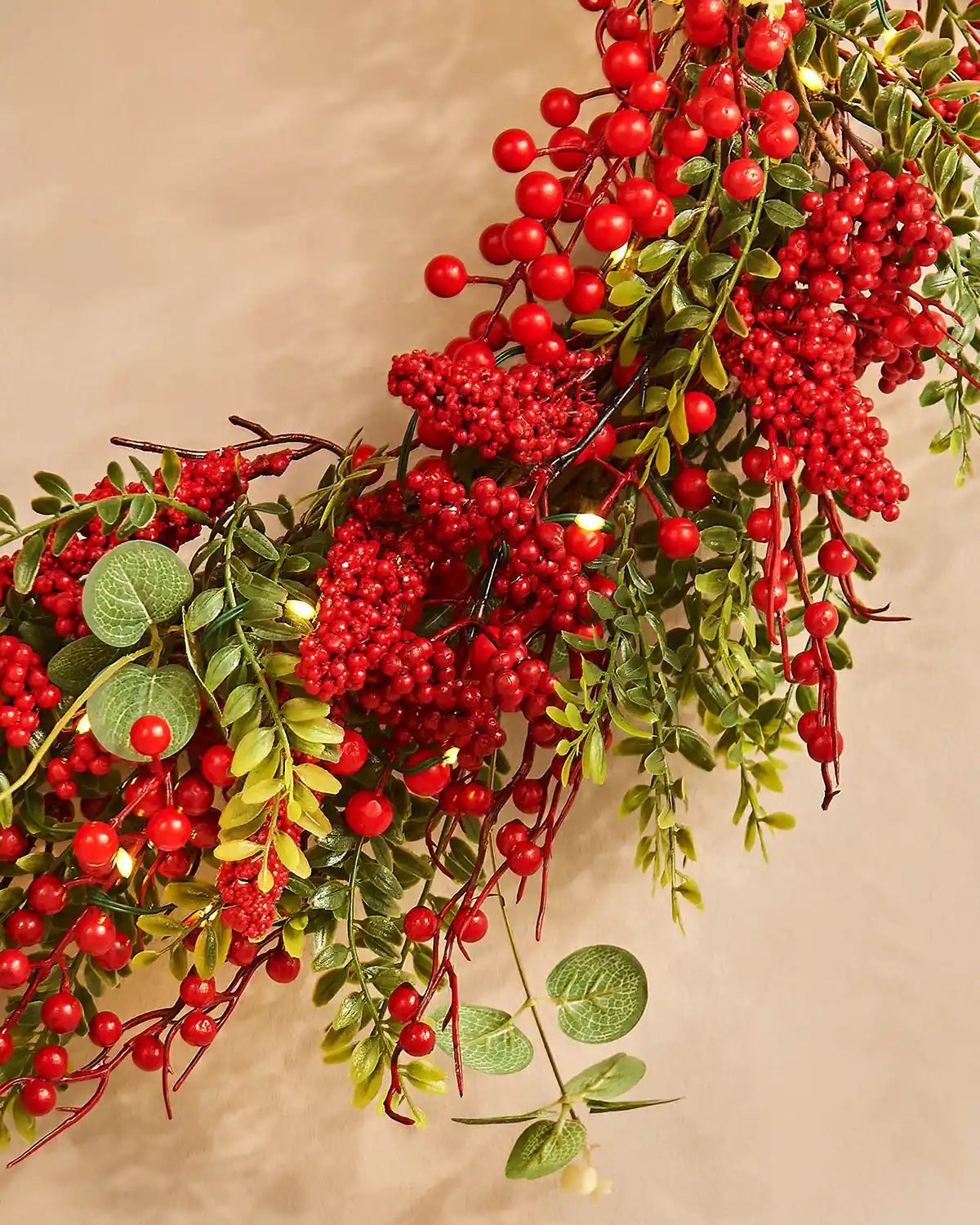 Decorative wreath with red berries and green leaves on a beige background