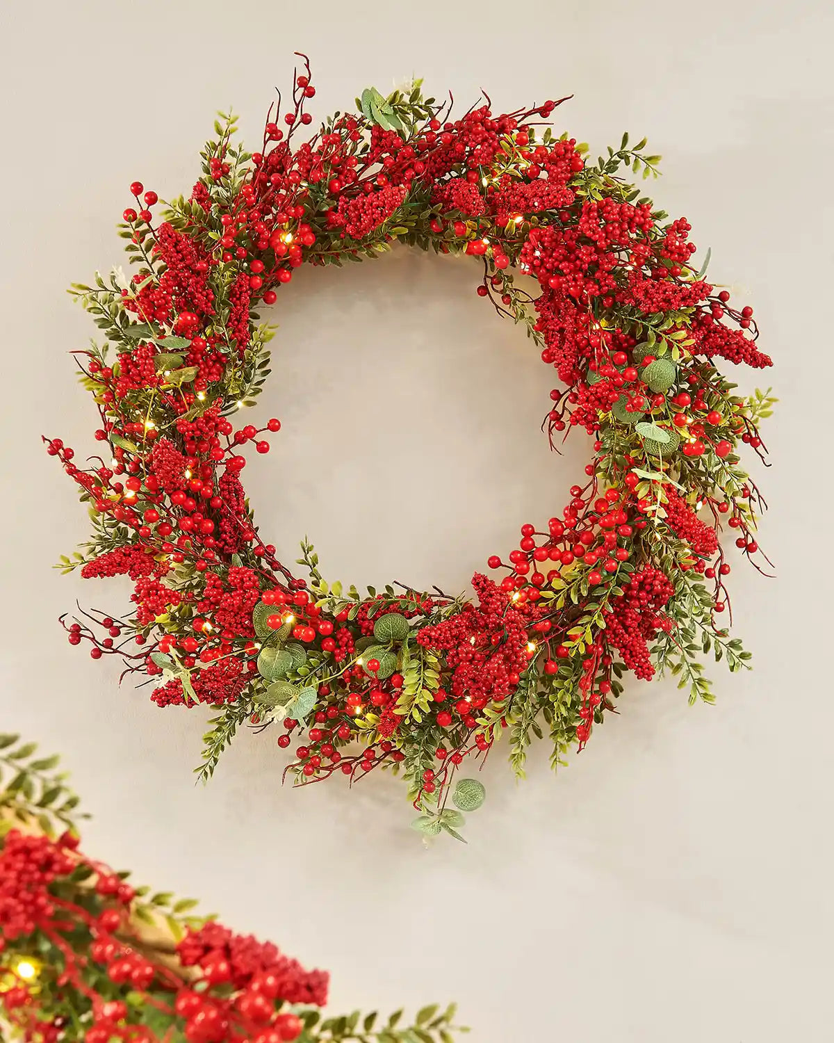 Decorative wreath with red berries and green leaves on a plain background