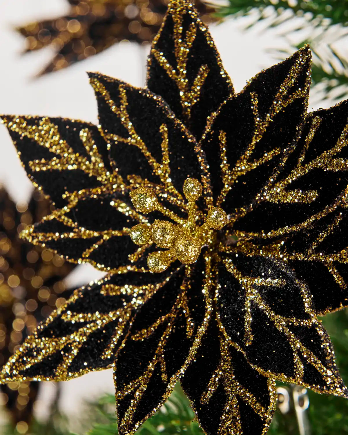 Detailed close-up of a black glitter poinsettia featuring gold glitter accents and a decorative gold beaded center
