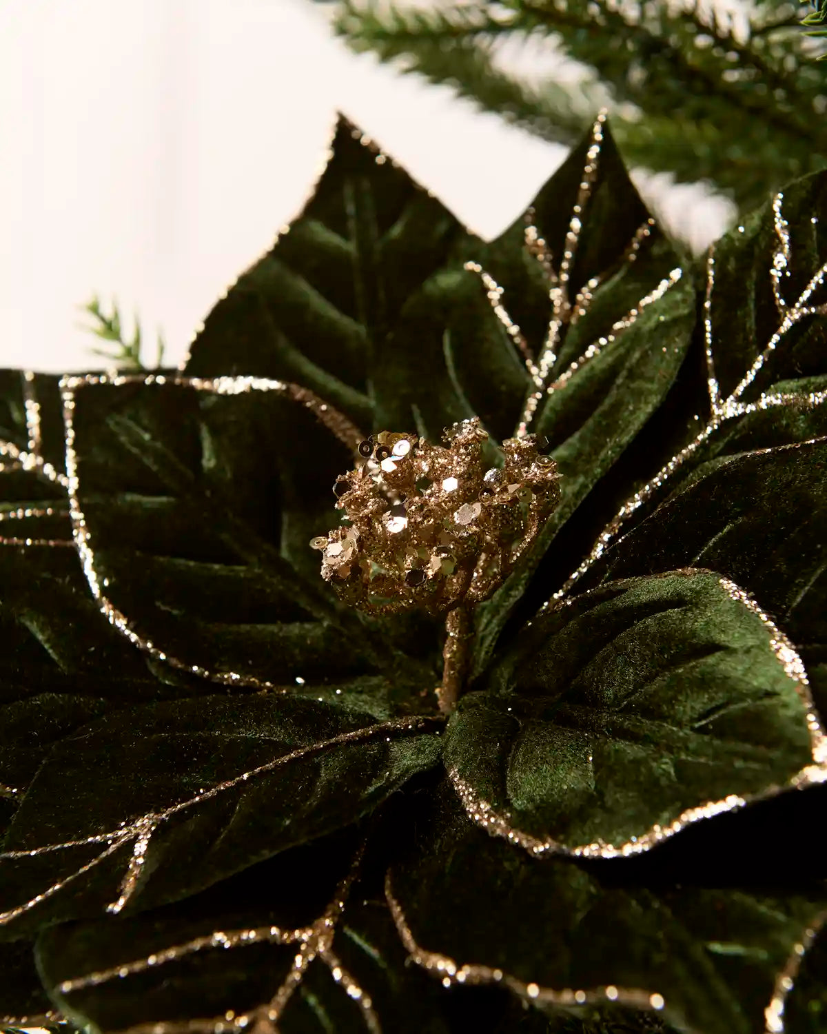 Detailed close-up of a sage green artificial poinsettia flower, showing its glittered green petals and sparkling gold sequin-covered center