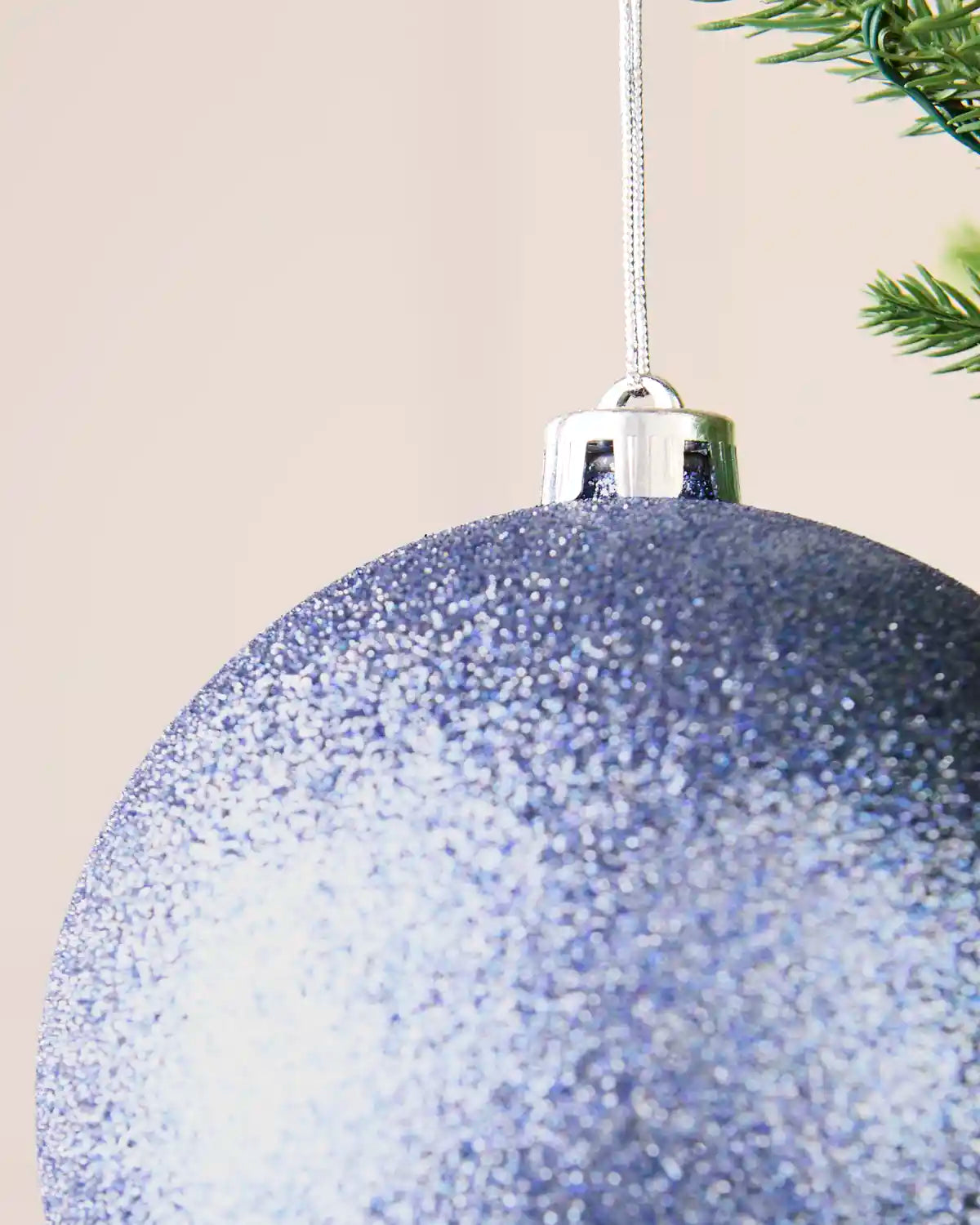 Detailed close-up of the ice blue 15 cm glitter shatterproof bauble with its silver cap and matching hanging string.