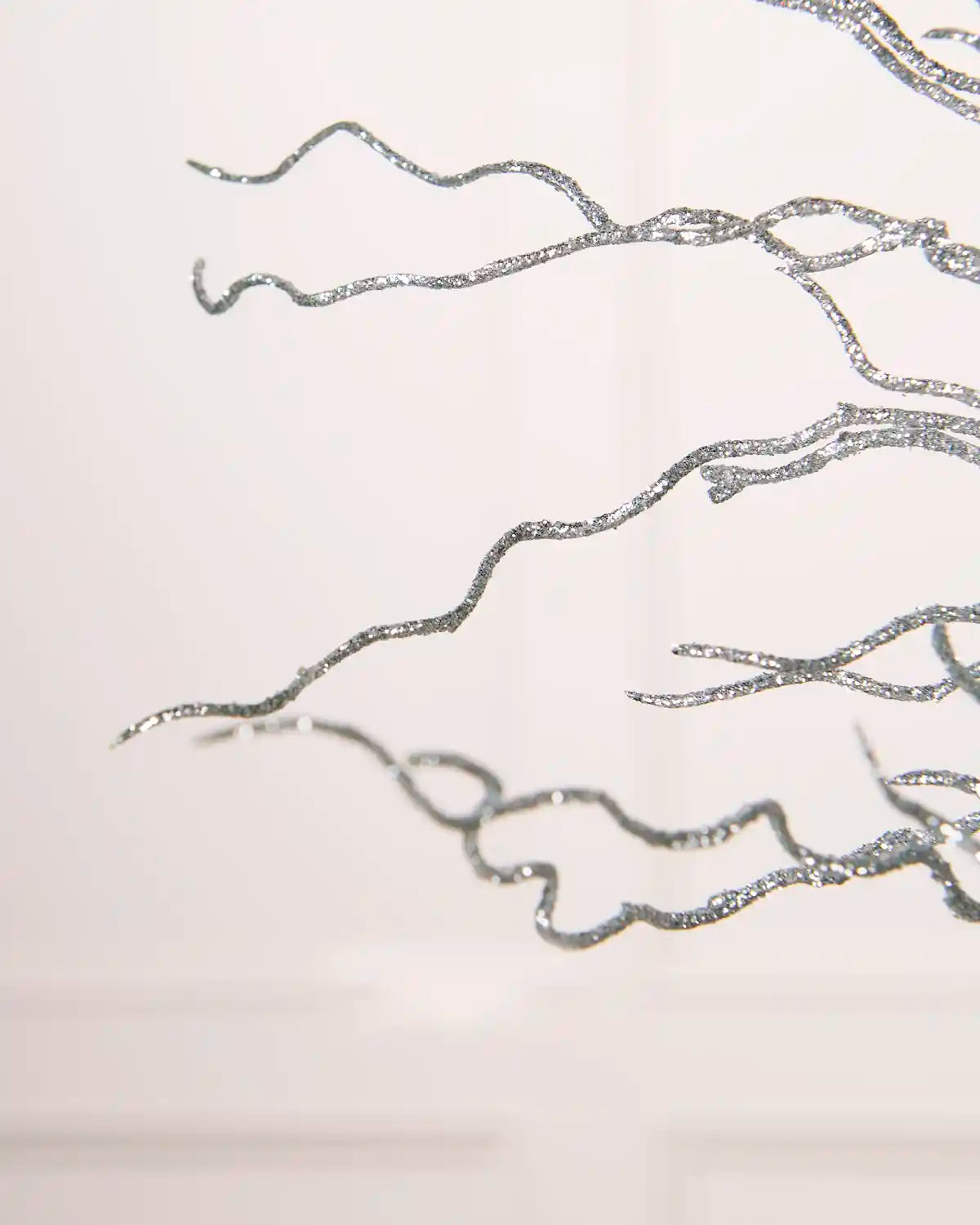 Detailed close-up of the thin, twisted silver glittered branches of the Glitter Twig Tree Topper against a white background