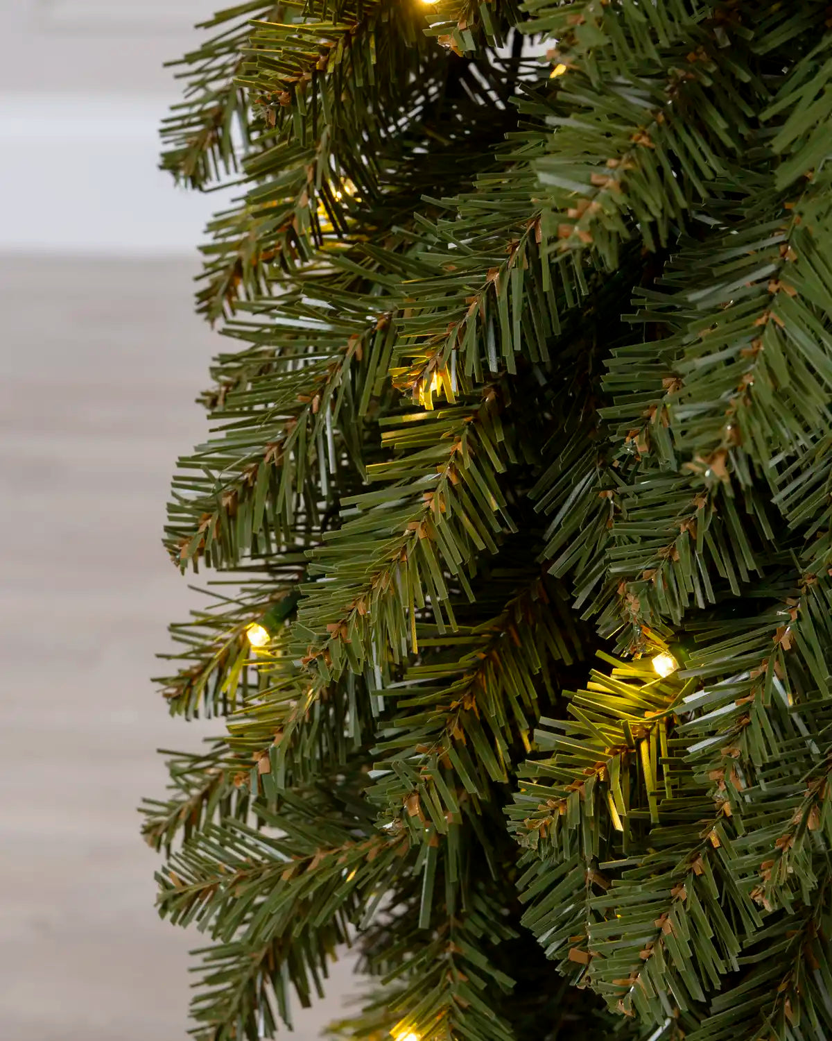 Detailed view of the green artificial branches and warm white lights on the slim Christmas tree