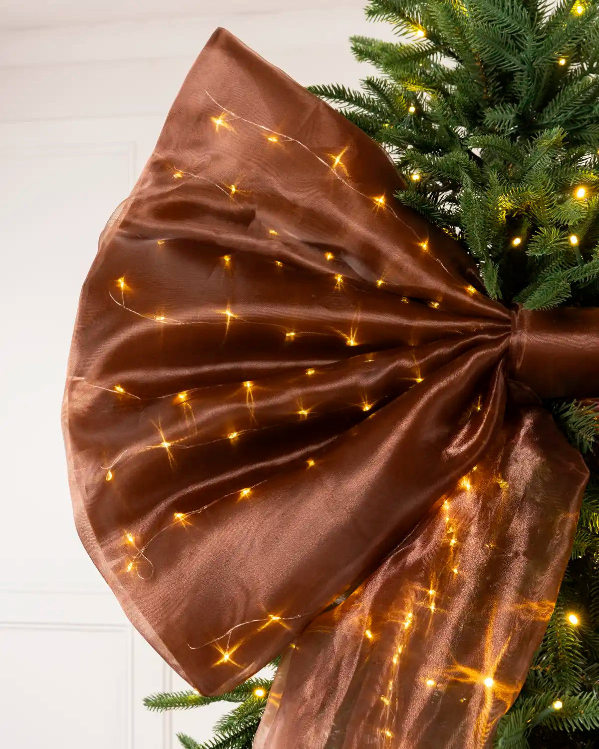 Detailed view of the large espresso brown bow and illuminated Christmas tree branches.