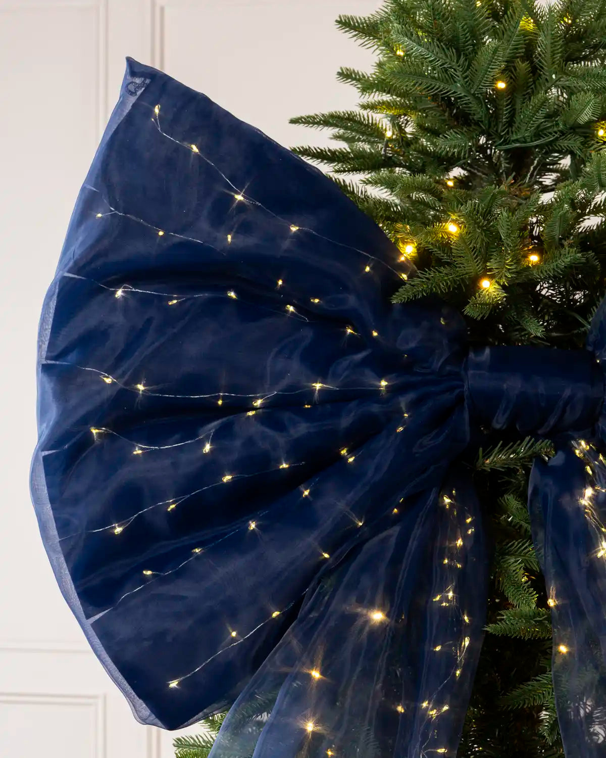 Detailed view of the large navy blue bow and illuminated Christmas tree branches.