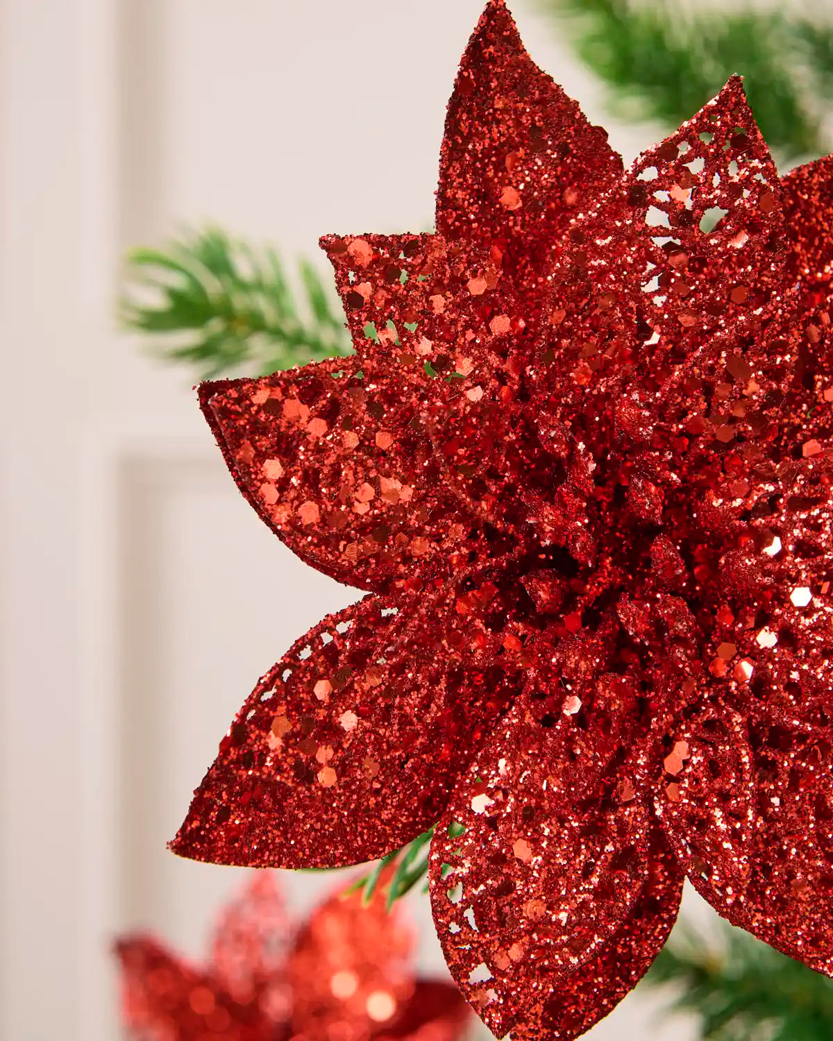 Detailed view of the red glitter artificial poinsettia flower, highlighting its layered petals and shimmering finish.
