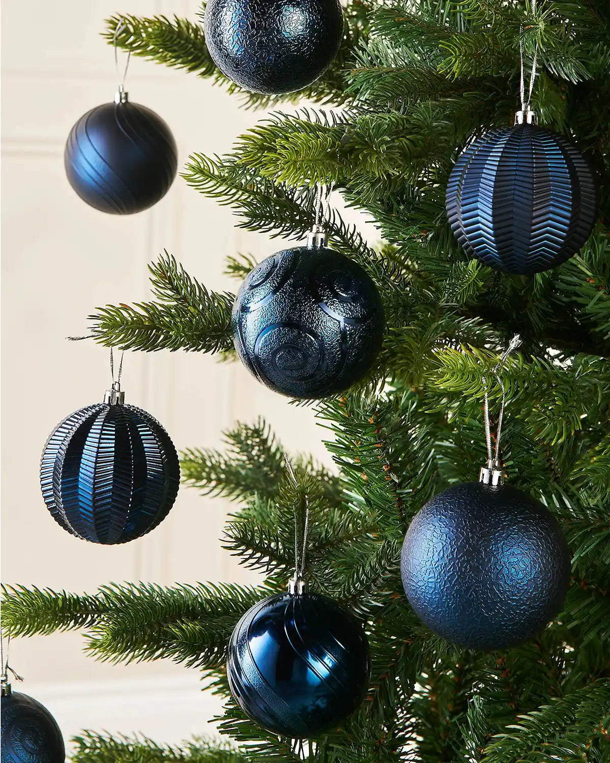 Eight Blue baubles on a Christmas tree branch against a cream wall