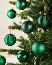 Eight Green baubles in various textures on s Christmas tree branch on a cream wall 