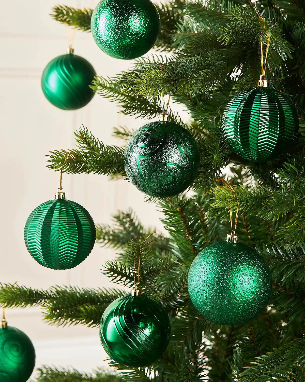 Eight Green baubles in various textures on s Christmas tree branch on a cream wall 