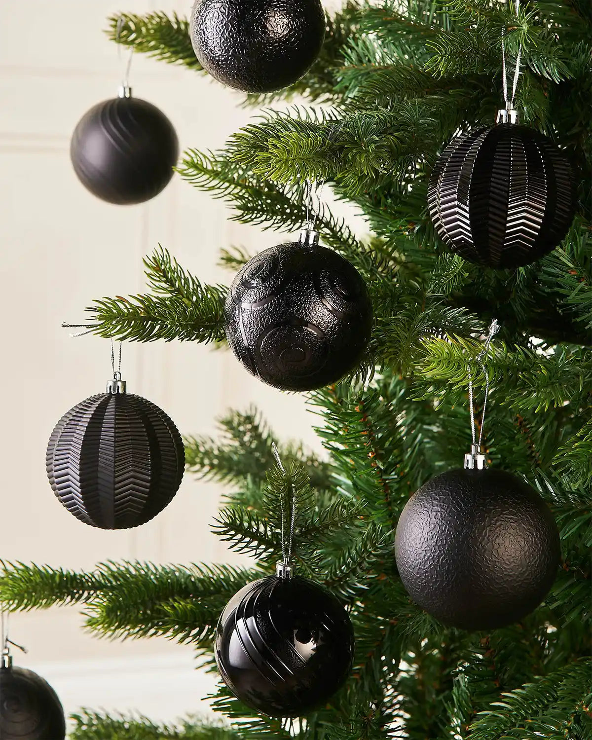 Eight black baubles on a Christmas tree branch against a cream background