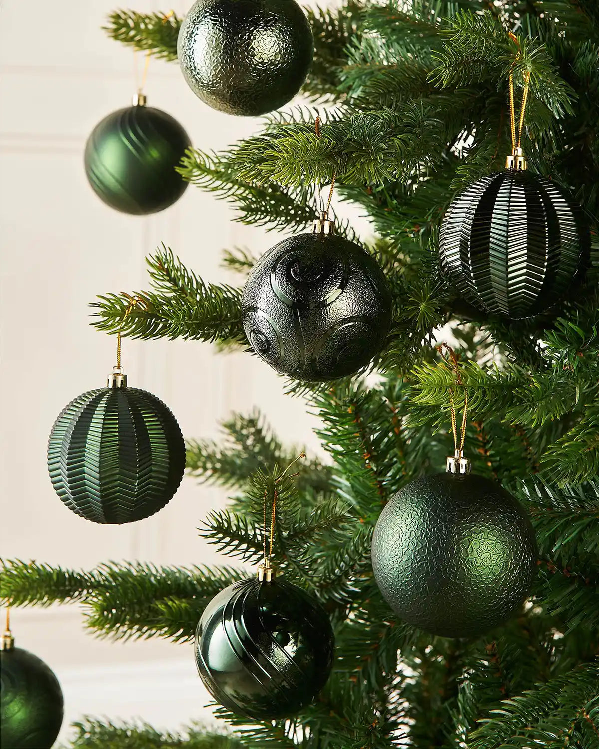 Eight sage green baubles in various textures on a Christmas tree against a cream wall